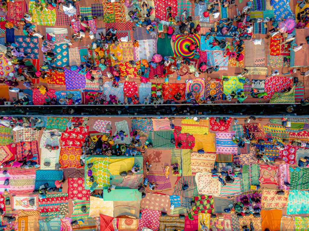 Home Aerial view of a vibrant textile market with colorful blankets and people, creating a lively patchwork.